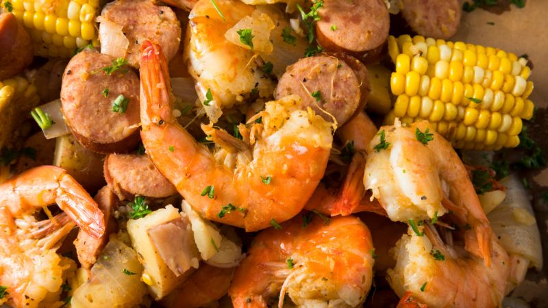 A seafood boil with shrimp, sausage, corn, potatoes, and parsley.