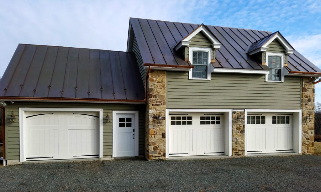 A green detached garage with three white garage doors.
