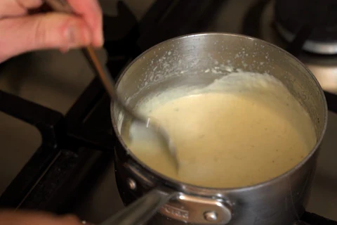 Someone stirs a light sauce in a small saucepan on the stove.