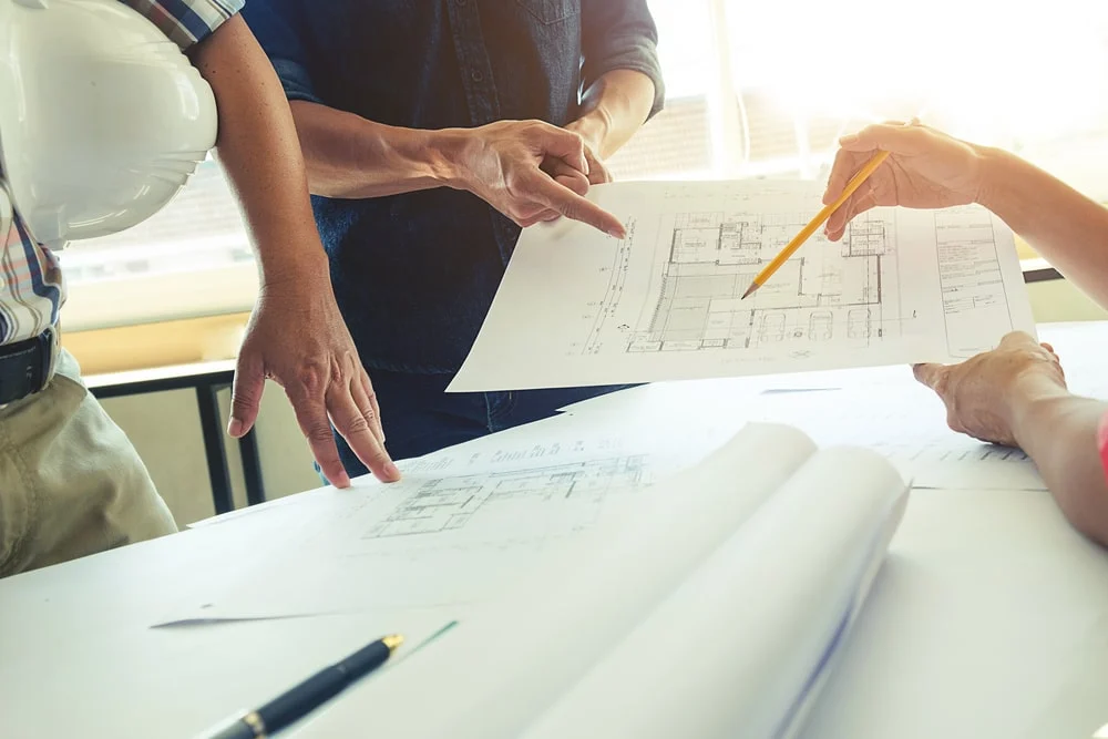 Three people working on an architectural plan.