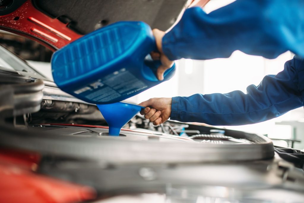 Auto mechanic pouring oil into funnel during an oil change