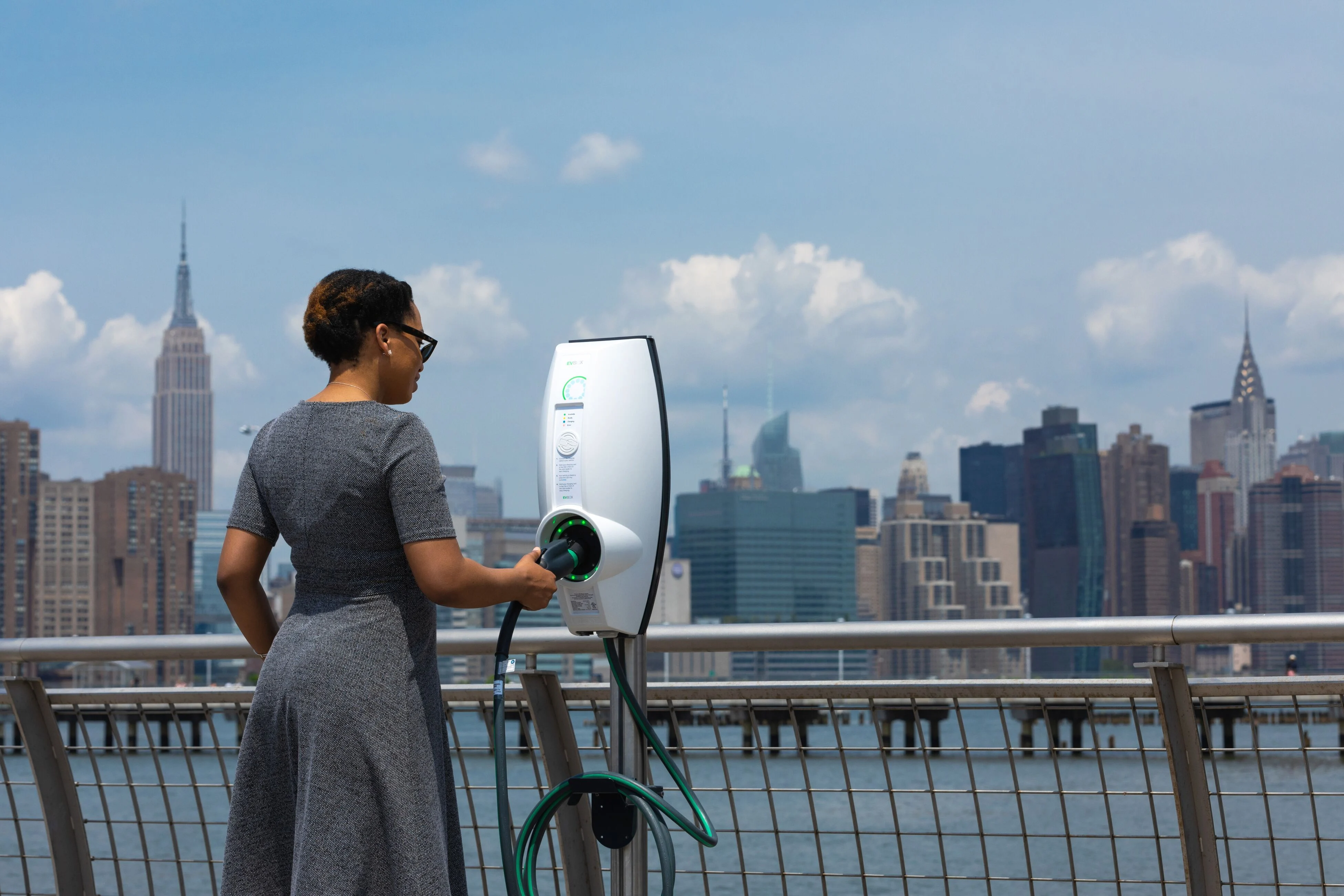 A woman holding an EVBox charging plug with New York City in the background.