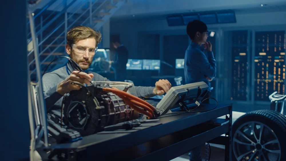 A battery engineer testing parts in a lab while wearing protective glasses.