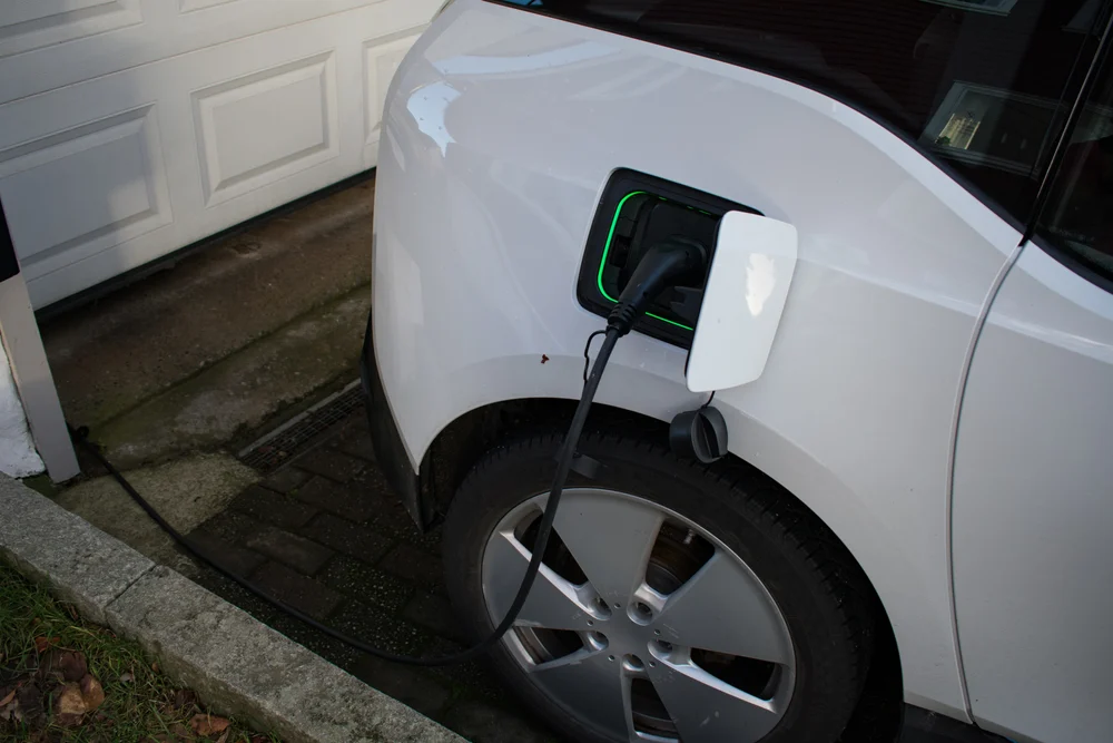 A closeup of an electric car charging on a driveway in front of a garage.