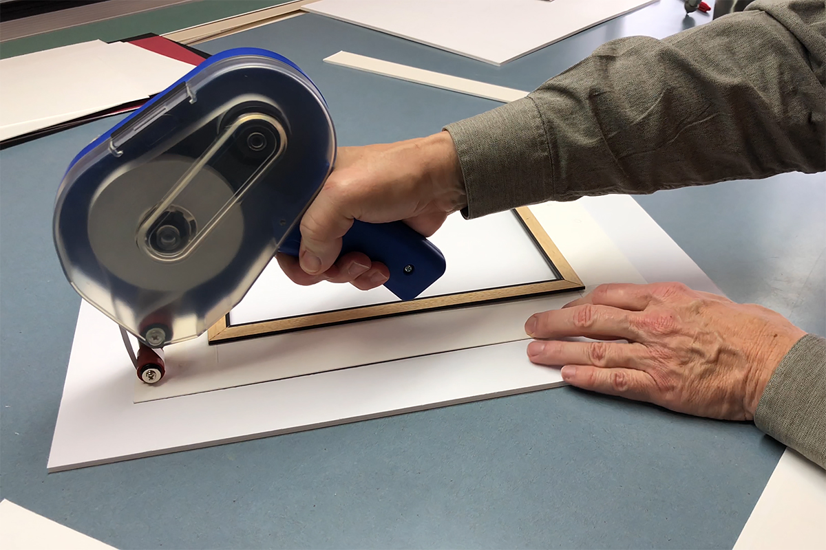 Adhering ProÂ® 410 ATG to the back of a mat board to apply foam core to level the back of mat surface.