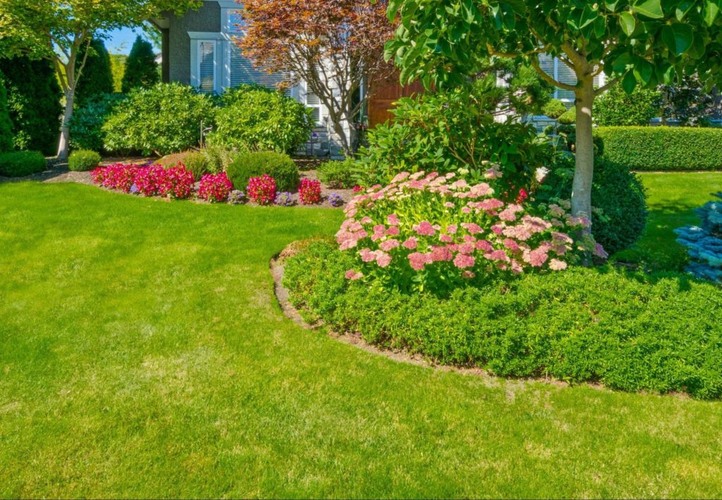 A tidy front yard featuring flowerbeds and trees.