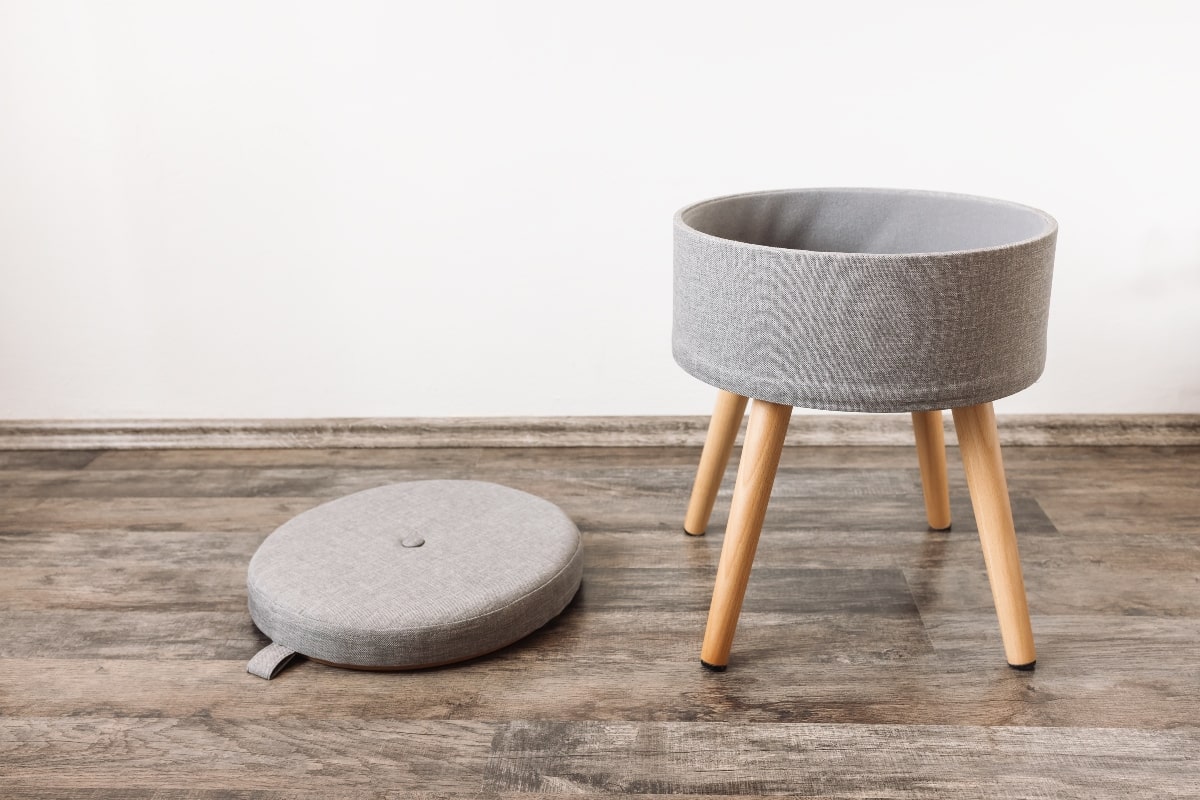 Compact storage furniture in the form of a grey fabric stool with hidden storage space under the removable lid, ideal for small home offices.