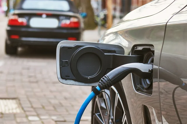 An electric car parked by the side of the road while being charged.