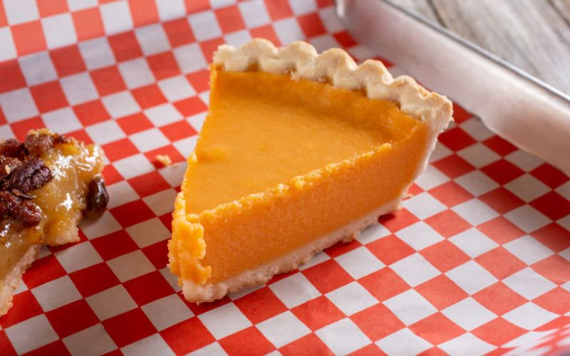 An orange pie slice on a red-and-white checkered surface. A bit of another dessert is visible on the left.