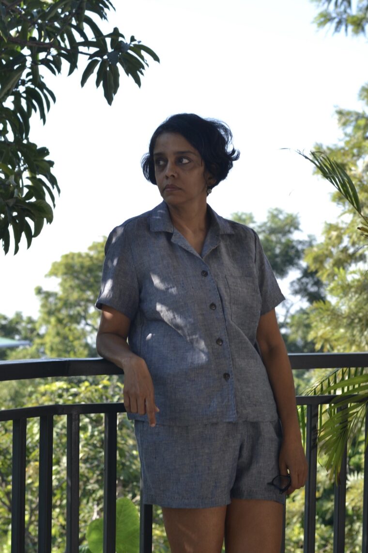 Woman leaning against a railing wearing a button-up pajama shirt and pajama shorts