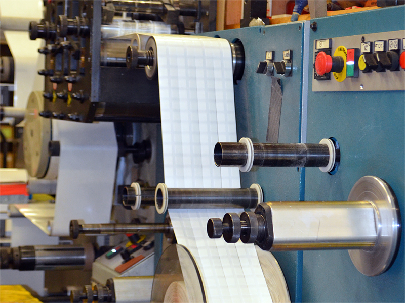 Rotary die cut machine shows the ability to slit die cut adhesive dash pieces in roll form.
