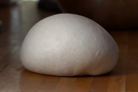 A smooth ball of risen dough sits on a wooden surface.