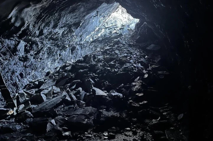 A large pile of rocks in the collapsed tunnel highlighted by light coming from a gap in the tunnel roof 
