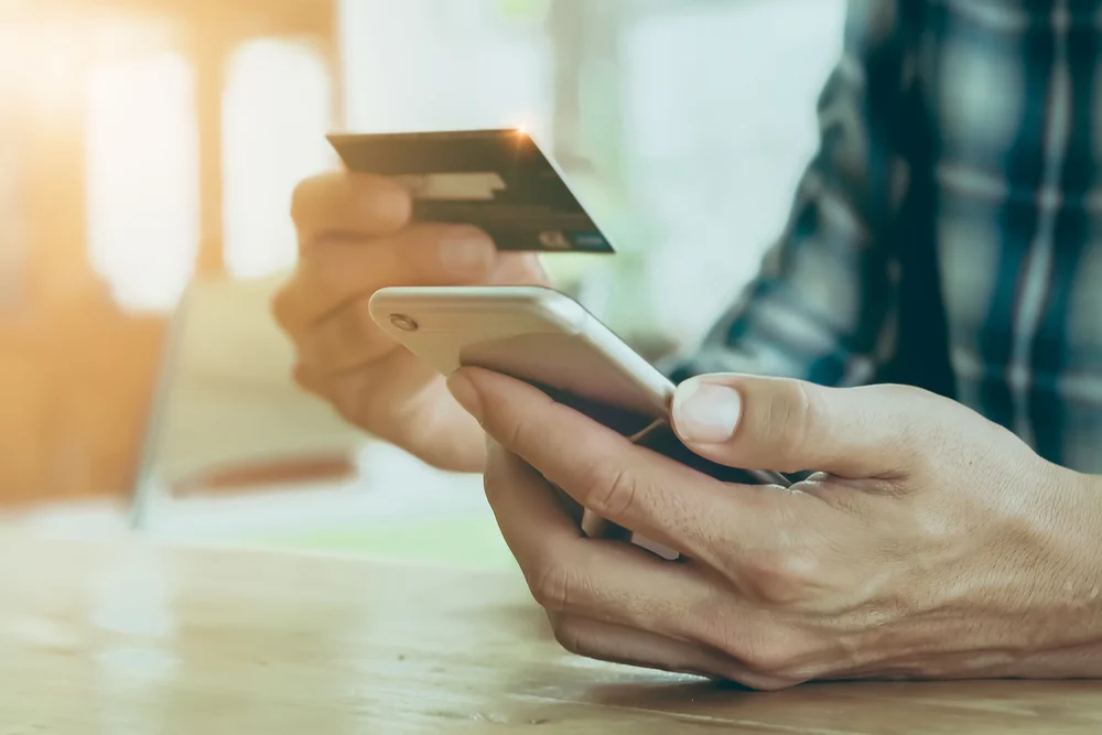 A man holding his phone in one hand and his credit card in the other.