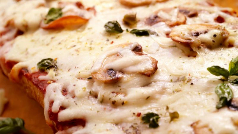 A close-up of a pizza with cheese, mushrooms, and basil.