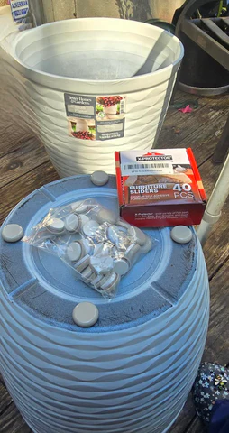 a large blue flower pot is flipped upside down showing the four gray gliders that have been attached, along with a baggie of more for other pots.