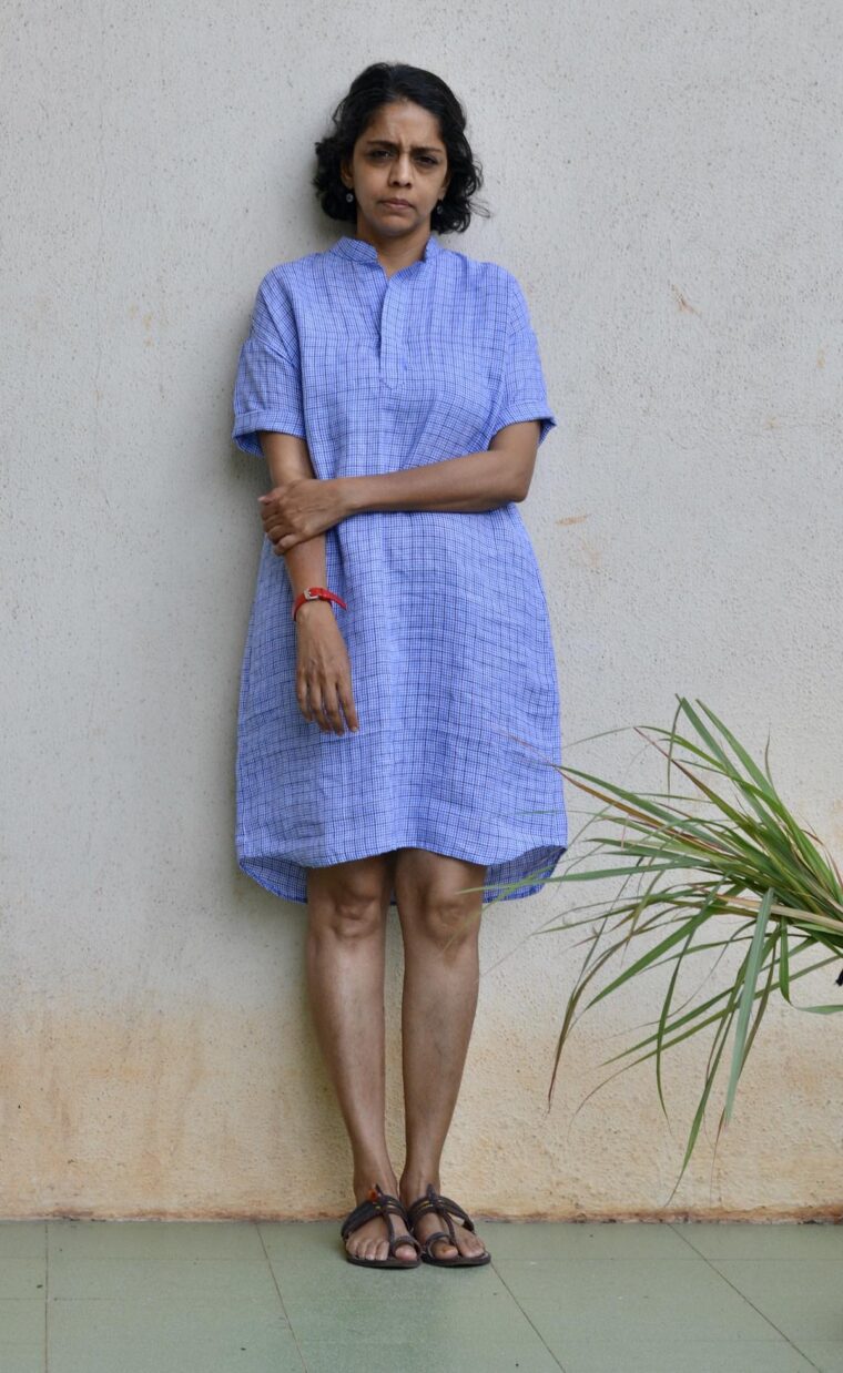 A woman wearing the blue linen Santa Rosa Dress. Sheâ€™s standing outside in front of a white wall.