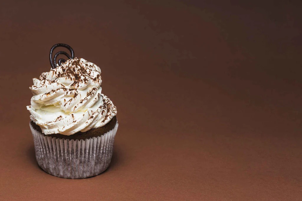 A chocolate cupcake with swirled vanilla frosting, topped with a chocolate spiral and cocoa dust, sits on a brown background.