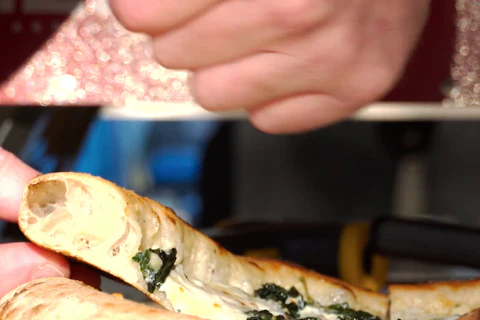 Close-up of hands slicing a spinach and cheese pizza.