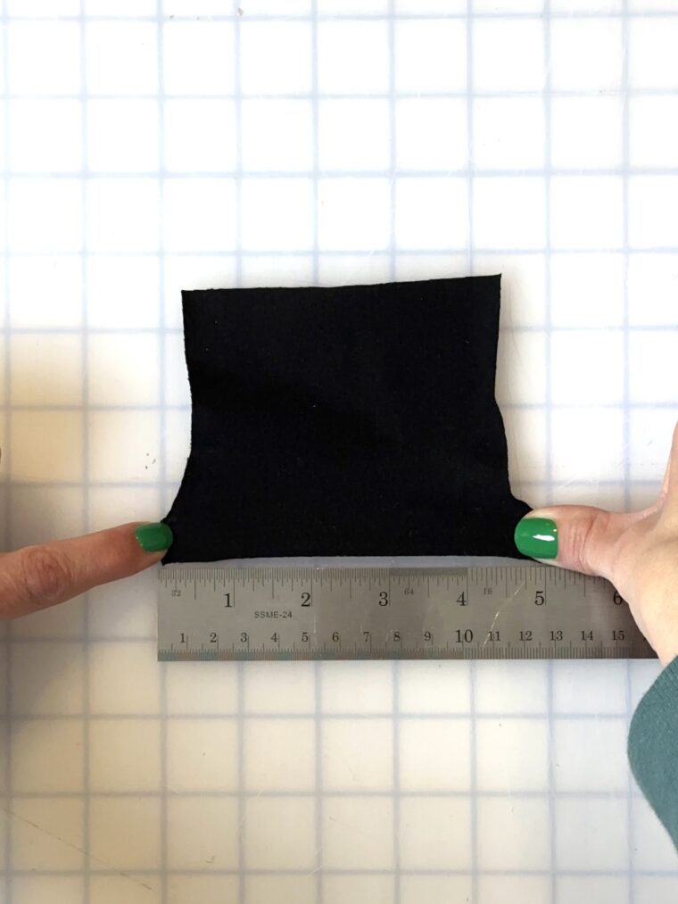 A square of black knit fabric stretched to 5 inches wide. A silver ruler is placed beneath the fabric showing the measurement.