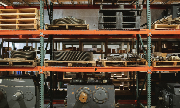 Industrial warehouse shelves with various sizes of gears and gearboxes stored.