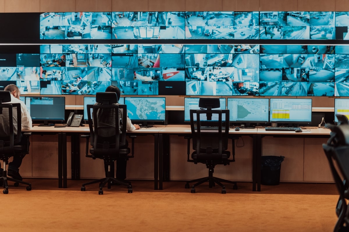 Security professionals working in a control room, using drafting chairs to maintain comfort and posture while monitoring security feeds across multiple screens.