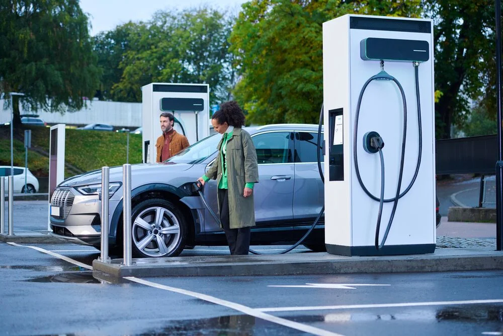 A man and woman standing beside an EV as the woman charges it using an EVBox Troniq Modular charging station.