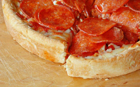 A close-up of a deep-dish pepperoni pizza with one slice slightly separated on a wooden surface.