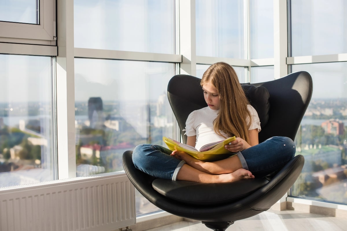 A young girl reading in a spacious black chair, illustrating the functional design of crossed leg office chairs for casual and focused activities.