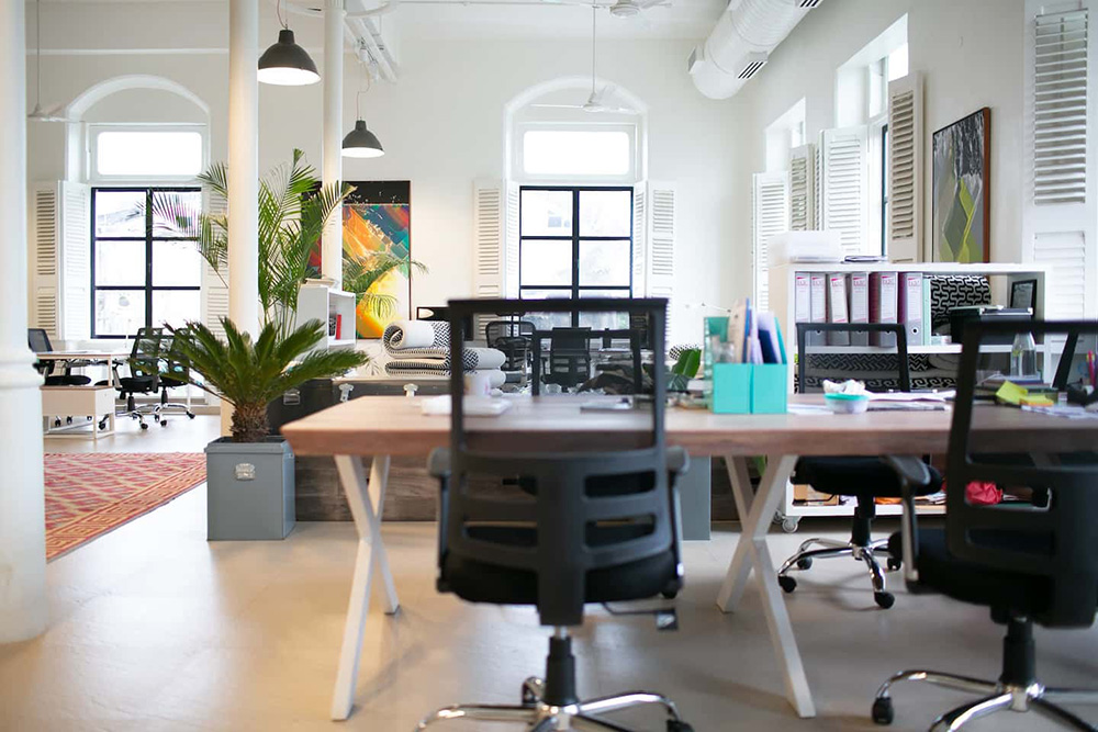 An open-plan office with wooden bench desks and ergonomic mesh-back chairs