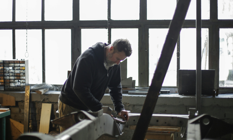 A man wearing a black sweatshirt fixes machinery in a factory.