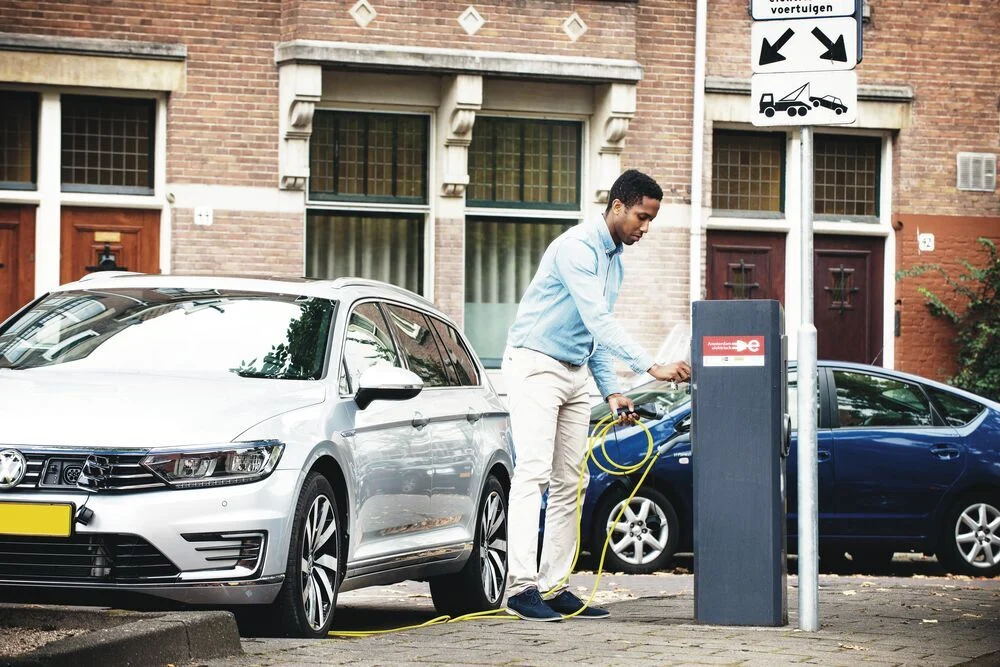 A young man in casual attire plugs in an electric vehicle on a street in Amsterdam.