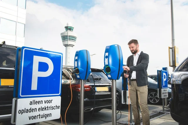 A man standing in front of a public EV charging station and inserting his car's charging cable.