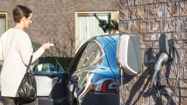 A woman entering her electric vehicle at her house, the exterior of the wall has an EVBox Elvi home charging station.