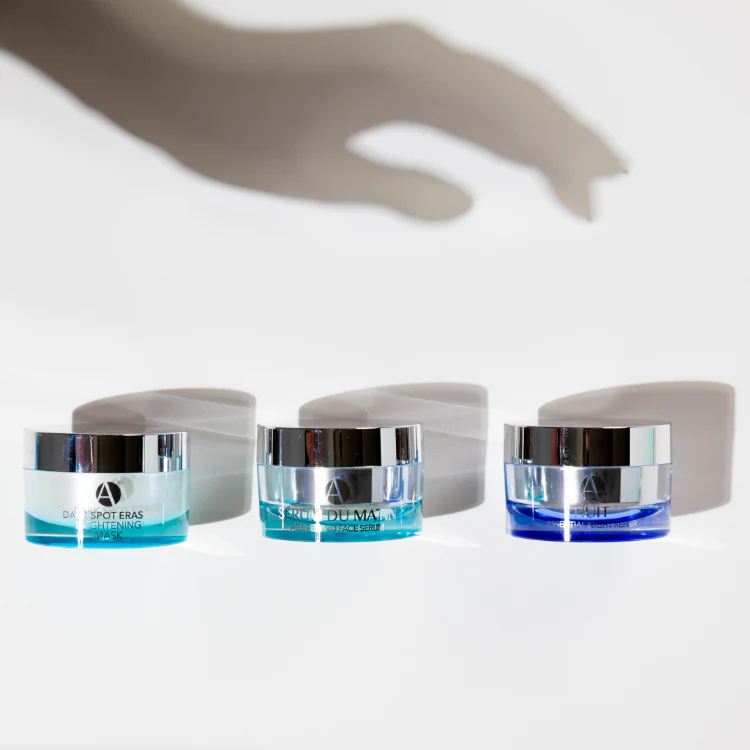 Shadow of a hand reaching to grab one of three ANJALI MD skincare products