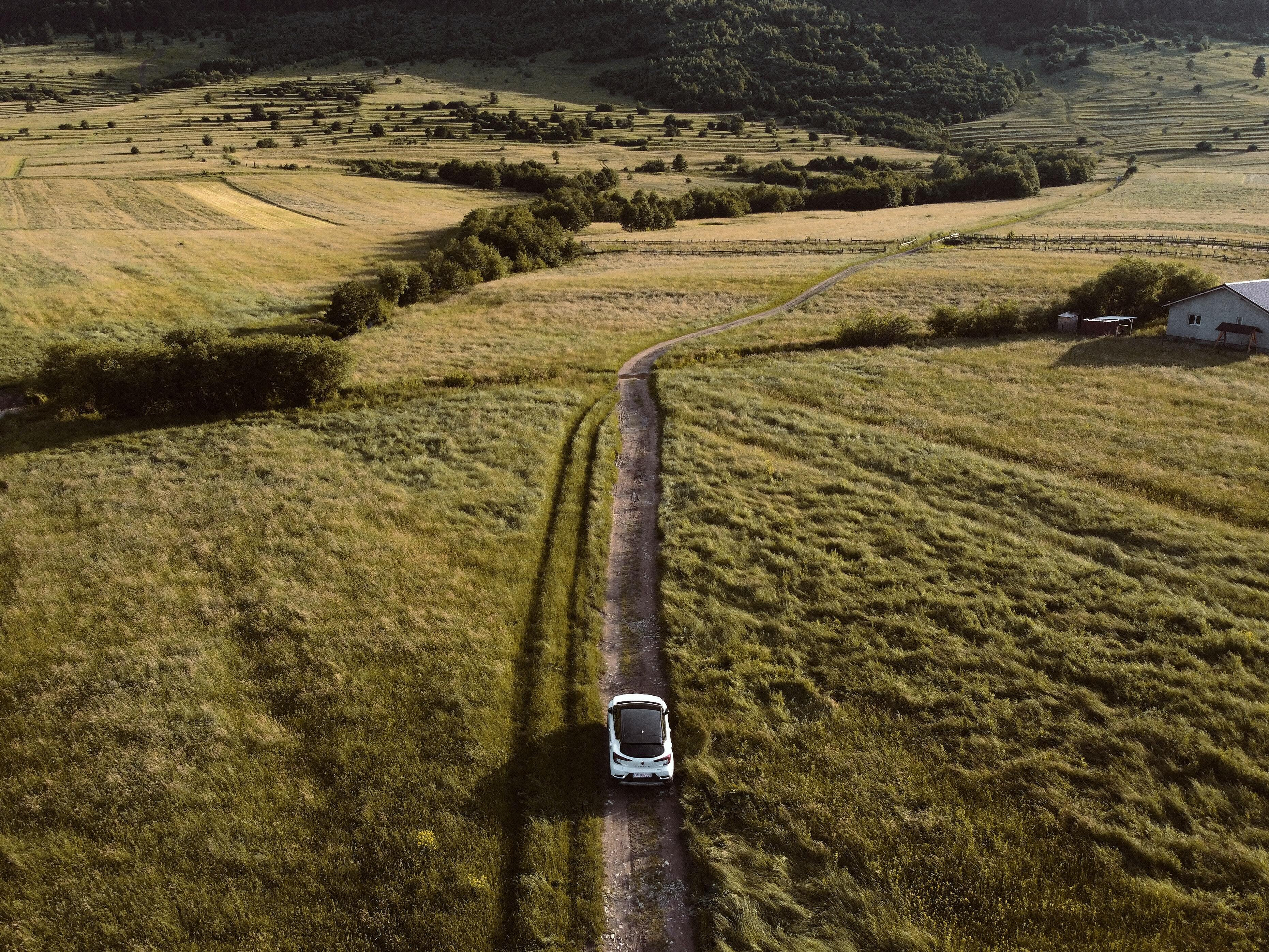 An aerial view of an electric car driving on an off-road path surrounded by lush countryside.
