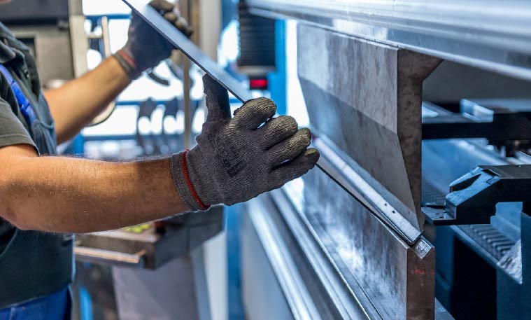 Man wearing a safety vest and safety gloves works on mechanical equipment.