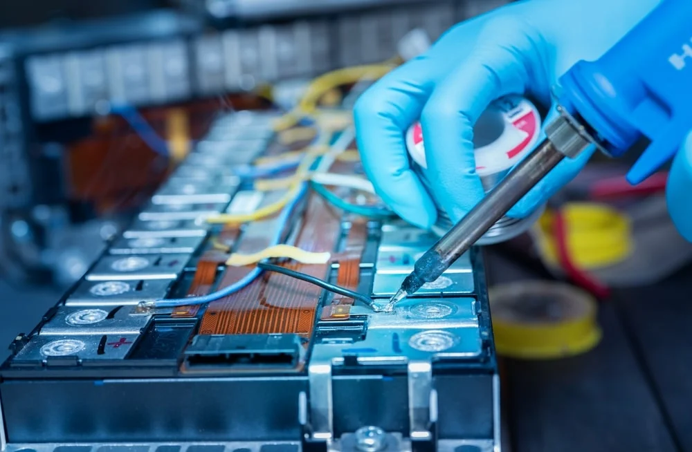 A battery manufacturer tinkering on a bare battery pack with specialized tools while wearing protective gloves.  