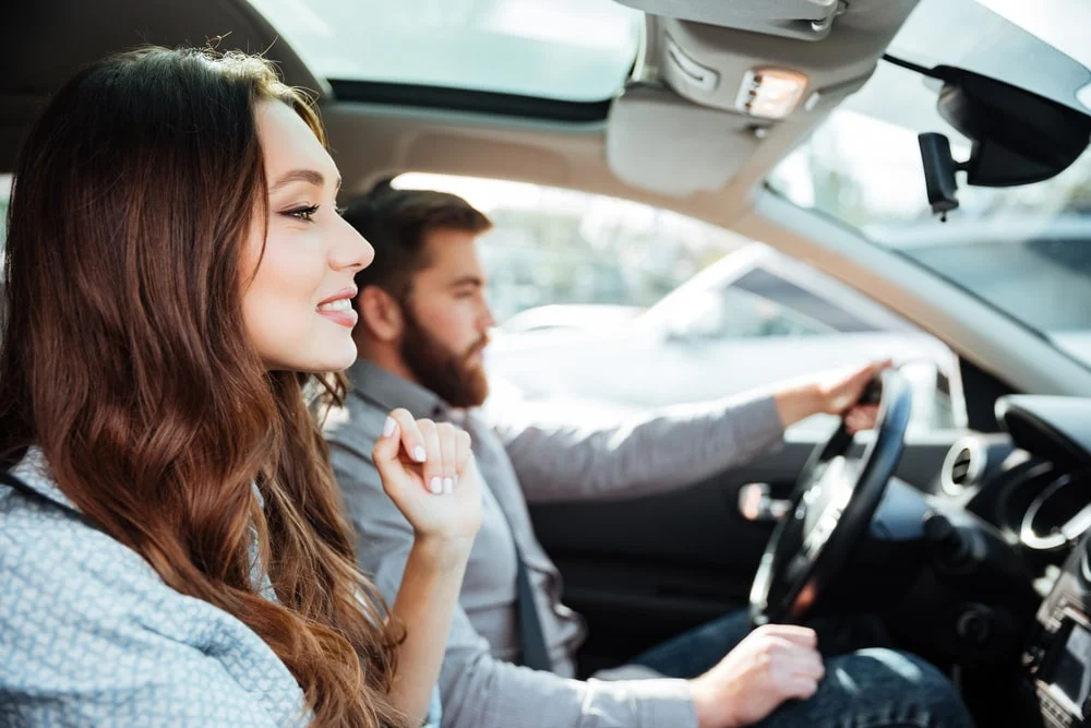 A man driving an EV with a woman sitting in the passenger seat.
