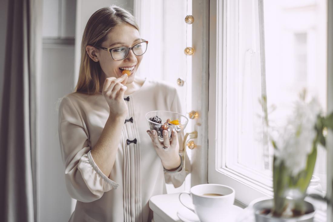 a woman looking out of a window and eating dried fruit.