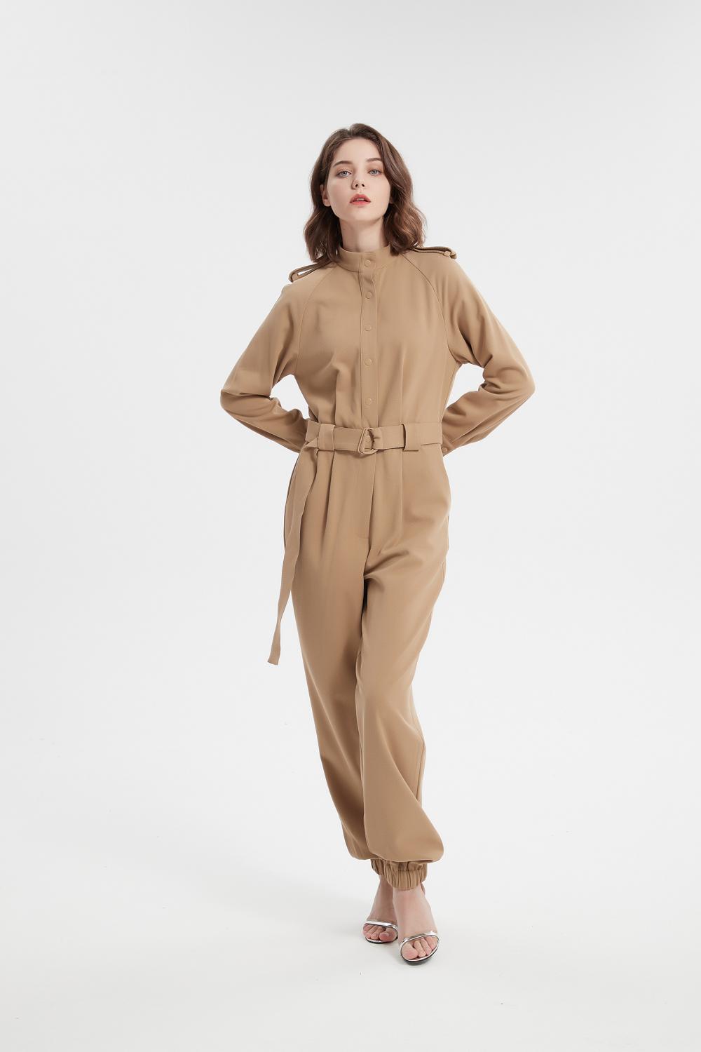 Mädchen gegen den Langarm -Jumpsuit mit Gürtel, den Jumpsuit mit Langschläfen.