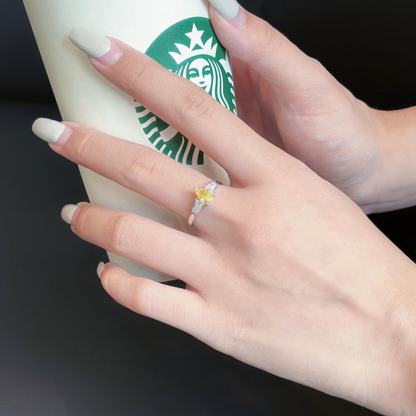 Anillo de tres piedras con diamantes de laboratorio de pera amarilla y baguettes cónicas que se muestran en la mano