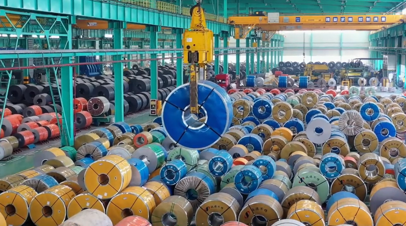 Eurocrane heavy-duty overhead crane with specialized vertical slab clamp lifting metal plates in steel manufacturing plant