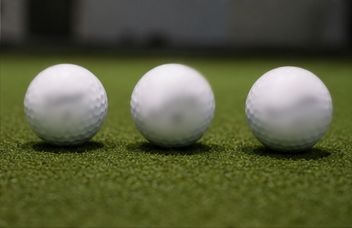 Three golf balls lined up on synthetic turf