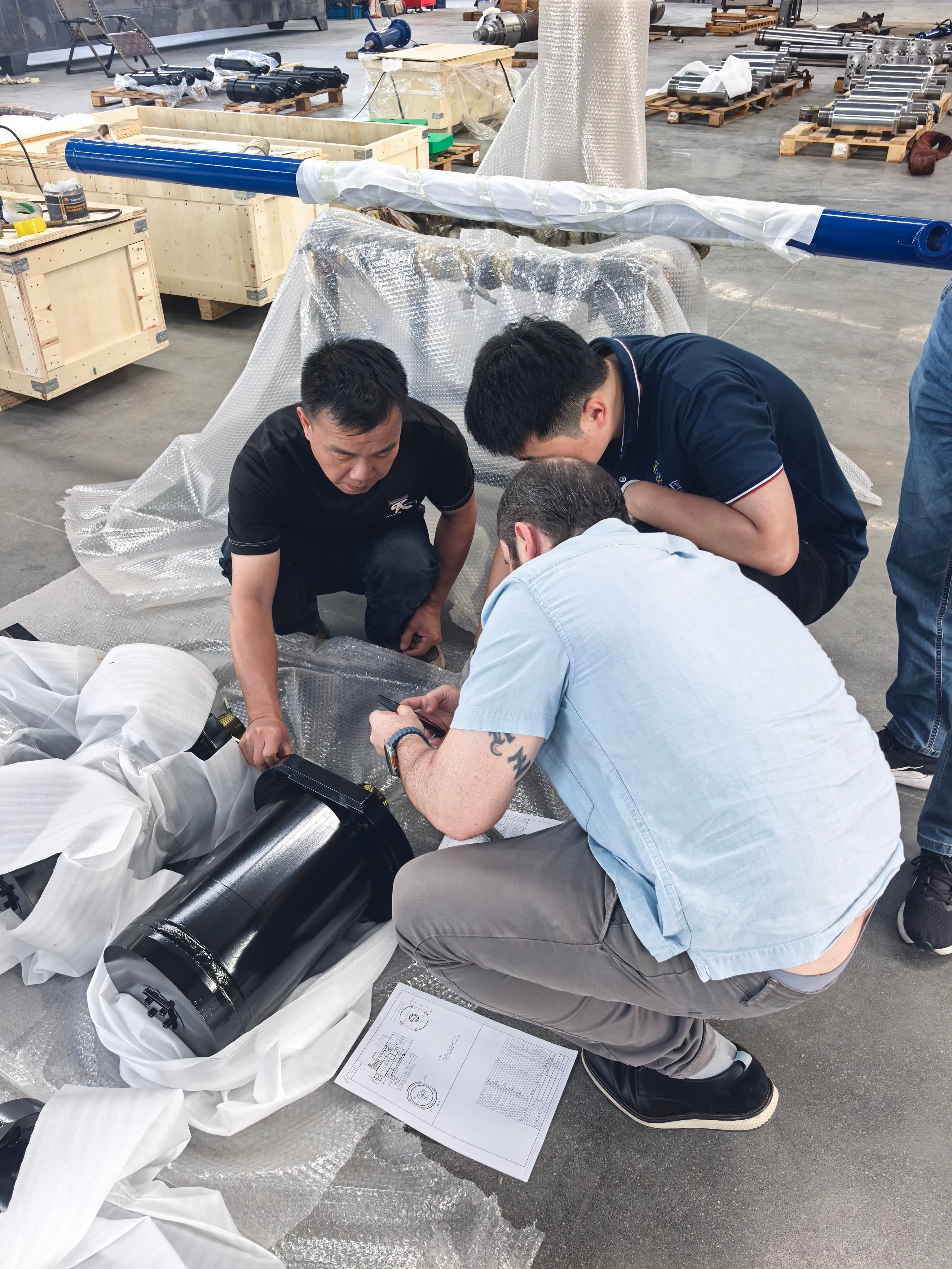 Brazilian client and technical team inspecting custom heavy-duty hydraulic cylinders and reviewing engineering drawings at Guoyue workshop.