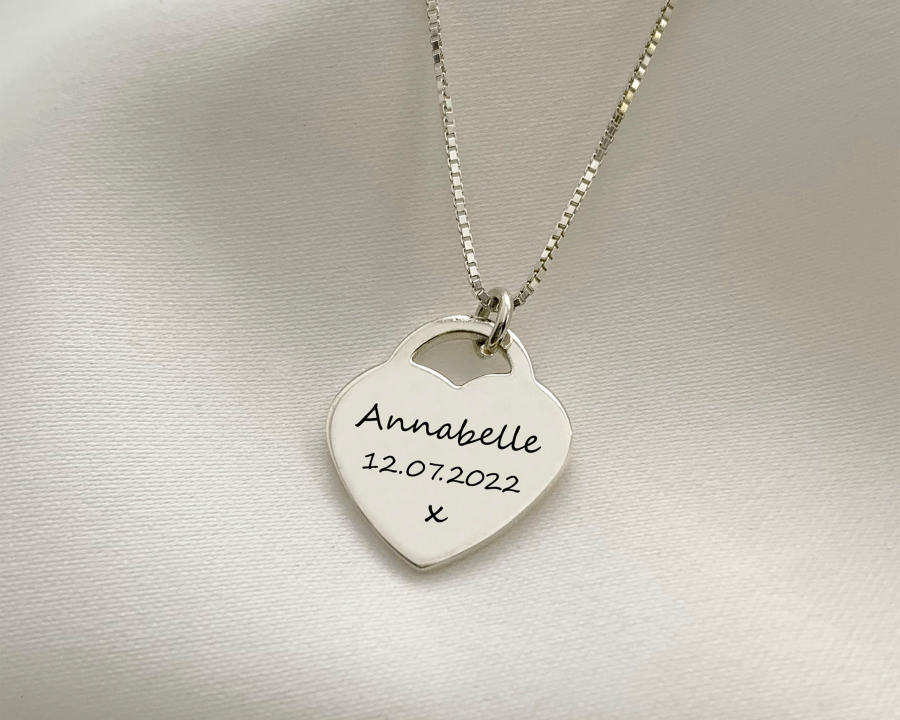 Colgante en forma de corazón grabado con un nombre y una fecha sobre una amplia superficie de metal.